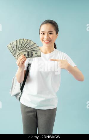 Stupito studente di ragazza che punta il dito indice su se stesso tenere ventilatore di banconote in dollari Foto Stock