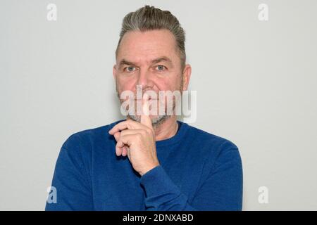 Uomo di mezza età che fa un gesto frettoloso alzando il dito a. le sue labbra come chiede silenzio in una testa frontale e spalle ritratto Foto Stock