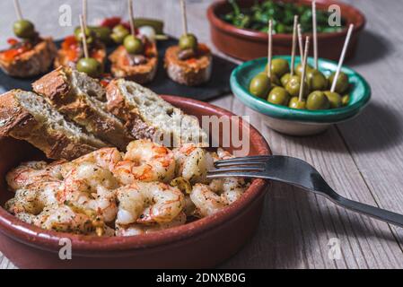 vista orizzontale ravvicinata di una casseruola con gamberi fritti con aglio e prezzemolo e altri piatti di tapas e una tazza di mer vino sullo sfondo Foto Stock