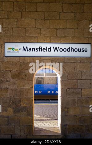 Segno sopra la stazione ferroviaria costruita in pietra, Mansfield Woodhouse, Nottinghamshire, Inghilterra, con un treno che passa da un arco aperto. Foto Stock