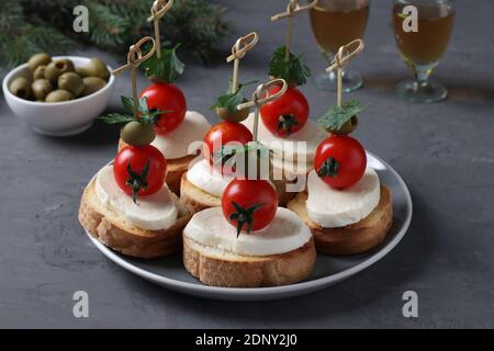 Crostini di mozzarella, pomodori ciliegini, olive verdi, prezzemolo su crostini di pane bianco su fondo grigio scuro. Spuntino festivo di Capodanno. Primo piano Foto Stock