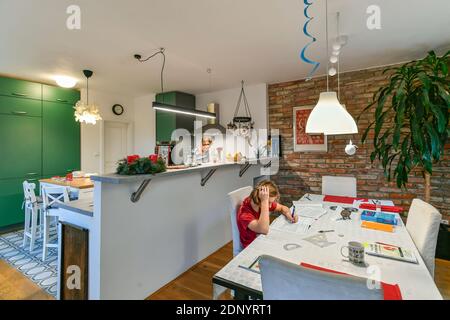 scolaro fa i suoi lavori in cucina mentre sua madre cuoce nel tempo di avvento Foto Stock