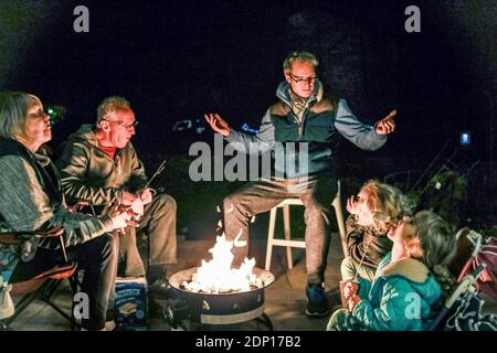 la famiglia si riunisce intorno a firepit fuori raccontare storie e mangiare Foto Stock