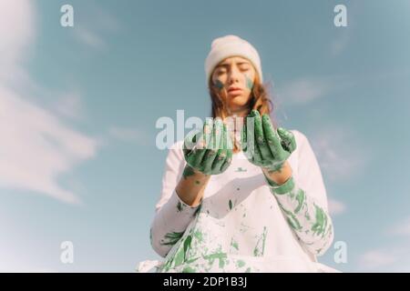Giovane donna che guarda giù sulle sue mani dipinte di verde Foto Stock