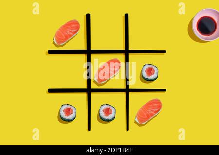 TIC-tac-TOE game con salmone sushi maki e nigiri con nero bastoncini di pollo su sfondo giallo Foto Stock