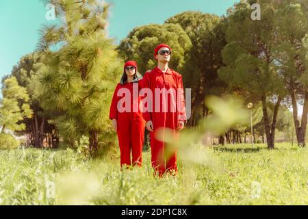 Giovane coppia che indossa tute rosse e cappelli in piedi in natura Foto Stock