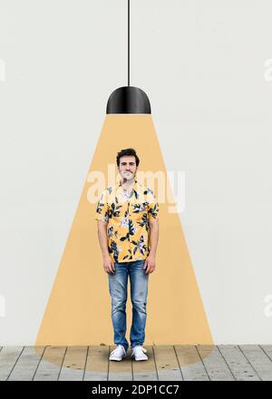 Giovane uomo in piedi sotto luce illuminata contro la parete Foto Stock