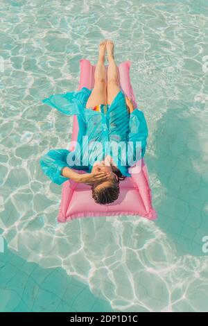 Donna che indossa un impermeabile blu che si rilassa sul letto d'aria rosa piscina Foto Stock