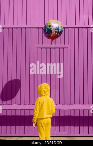 Vista posteriore dei bambini vestiti in giallo che tengono il pallone dentro parte anteriore dello sfondo viola Foto Stock