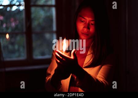 Donna che tiene il matchstick bruciante luminoso mentre in piedi nel buio a. casa Foto Stock