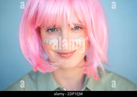 Giovane donna con parrucca rosa, lettere sul viso, libertà Foto Stock