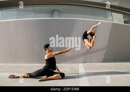 Ballerina femminile che fa acrobat mentre ginnasta maschile che pratica il salto di stag da parete grigia Foto Stock