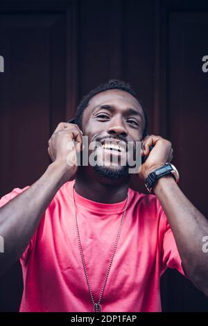 Ritratto di un uomo felice che indossa una t-shirt rosa ascoltando la musica con cuffie Foto Stock