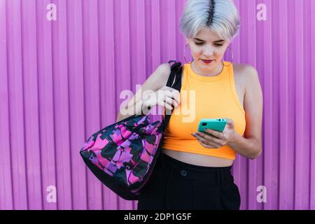 Ritratto di donna dal look moderno e telefono cellulare con sfondo urbano viola a Granada, Spagna. Donna giovane bionda 'Gen Z' colorato cellulare Foto Stock