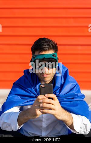 Uomo d'affari con smartphone con capo supereroe e occhiali VR Foto Stock