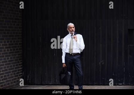 Ritratto di elegante imprenditore senior con i capelli grigi in piedi contro lo sfondo scuro Foto Stock