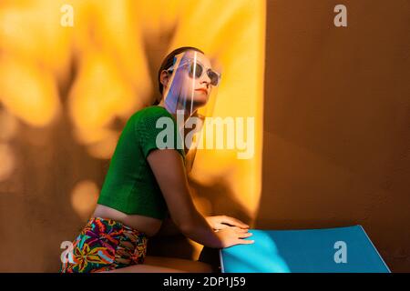 Donna in cortile colorato, indossare occhiali da sole uner viso scudo Foto Stock