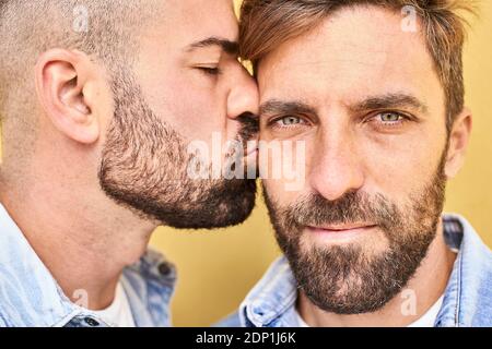 Primo piano di gay che baciano l'uomo mentre si trova contro il muro giallo Foto Stock