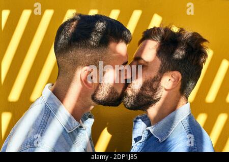 Gli uomini gay si baciano mentre si levano in piedi contro il muro giallo Foto Stock