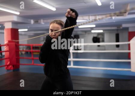 Donna determinata in nero sportswear facendo pugno jab mentre si pratica shadow boxing sul ring in palestra Foto Stock