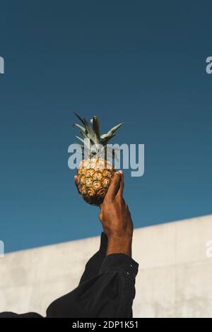 Primo piano dell'uomo che tiene un ananas sotto il cielo blu Foto Stock