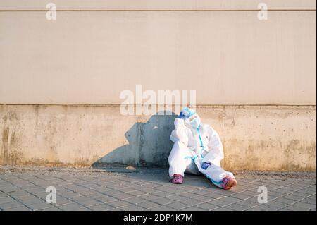 Infermiera femminile seduta con la testa in mano sul sentiero contro parete Foto Stock