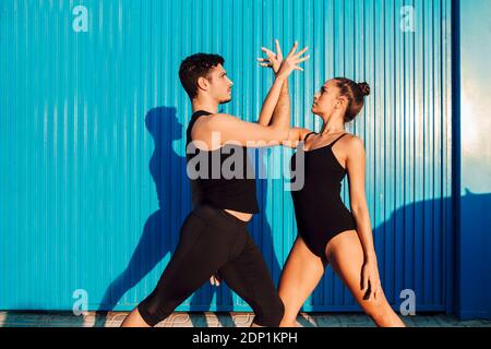 Giovane maschio acrobat aiutare ballerina femminile in posa dance by parete blu Foto Stock