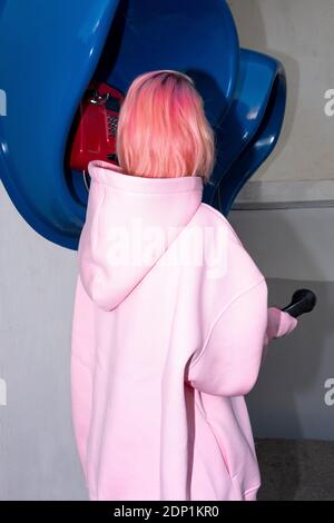 Vista posteriore della giovane donna con i capelli rosa che indossano il rosa camicia con cappuccio di fronte alle cabine telefoniche Foto Stock
