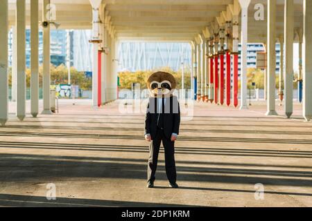 Uomo d'affari in abito nero con maschera meerkat all'aperto, Barcellona, Spagna Foto Stock