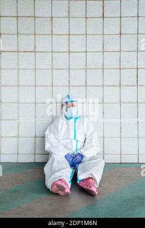 Infermiera femminile premurosa seduta contro la parete piastrellata Foto Stock