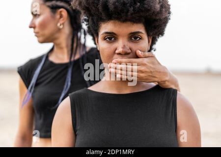 Donna di mano che copre la bocca di un'altra donna Foto Stock