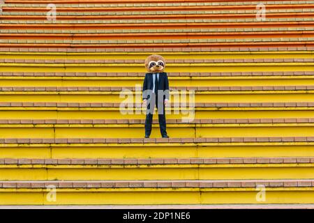 Uomo d'affari in abito nero con maschera di mierkat in piedi sulle scale Foto Stock