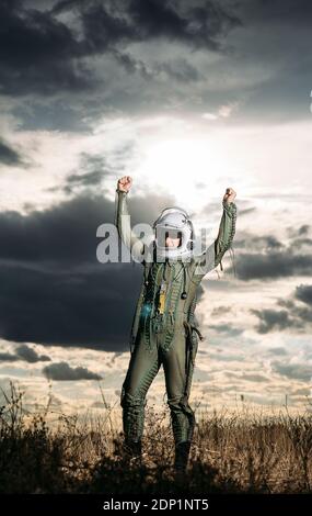 Ponendo l'uomo vestito come un astronauta su un prato con drammatica nuvole in background Foto Stock