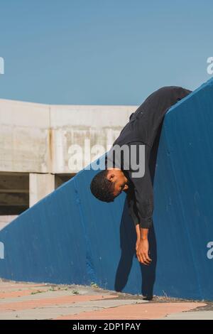 Giovane uomo che indossa kaftan nero sdraiato su muro blu Foto Stock