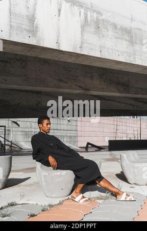 Giovane uomo che indossa kaftan nero rilassante su cemento stutture all'aperto Foto Stock