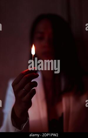 Donna che sta in piedi e che sta bruciando matchstick nel buio a casa Foto Stock