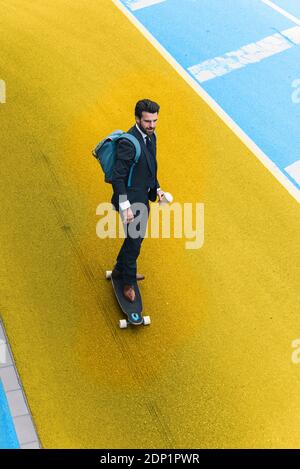 Skateboard giovane uomo d'affari su strada gialla e blu Foto Stock