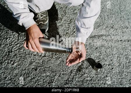 Uomo che versa l'acqua dalla thermos fiasca in un paesaggio arido Foto Stock