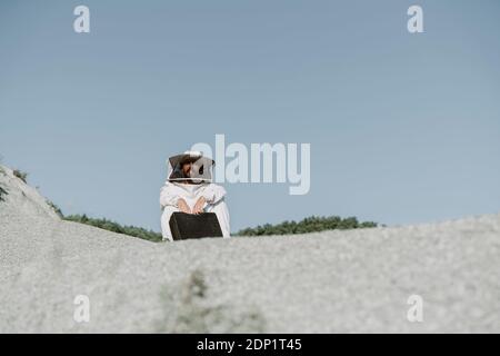 Uomo con valigia che indossa un abito da guardiano seduto Foto Stock