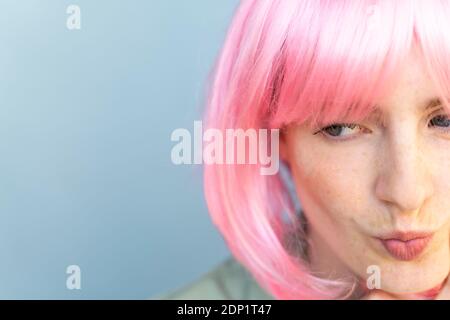 Ritratto di giovane donna che indossa la parrucca rosa che la indossa in bocca Foto Stock