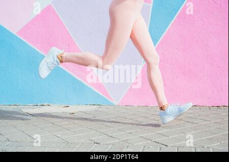 Gambe di donna che corre in città di fronte parete colorata Foto Stock