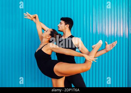 Giovane ginnasta maschile che aiuta la ballerina femminile bilanciamento da parete blu Foto Stock