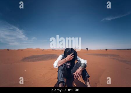 Uomo a mettere su il suo cappello nelle dune del deserto del Marocco Foto Stock