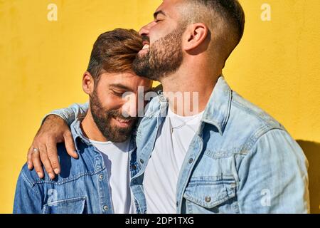 Couple smiling while standing with arm around against yellow wall Foto Stock