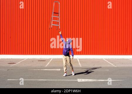 Giovane uomo che bilancia una scala di fronte ad un rosso parete Foto Stock