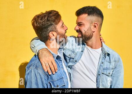 Coppia sorridente con braccio intorno guardarsi mentre in piedi contro la parete gialla Foto Stock