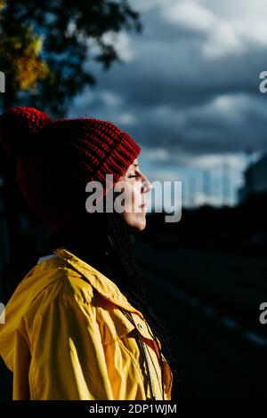 Contemplating woman with closed eyes standing on street during sunset Stock Photo