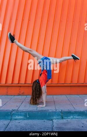 Giovane donna che fa la mano contro parete arancione Foto Stock