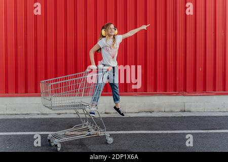 Ragazza con un carrello della spesa e orecchio defender nella parte anteriore della parete rossa Foto Stock