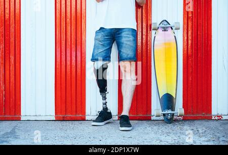 Giovane uomo con protesi di gamba in piedi accanto a skateboard a una parete Foto Stock